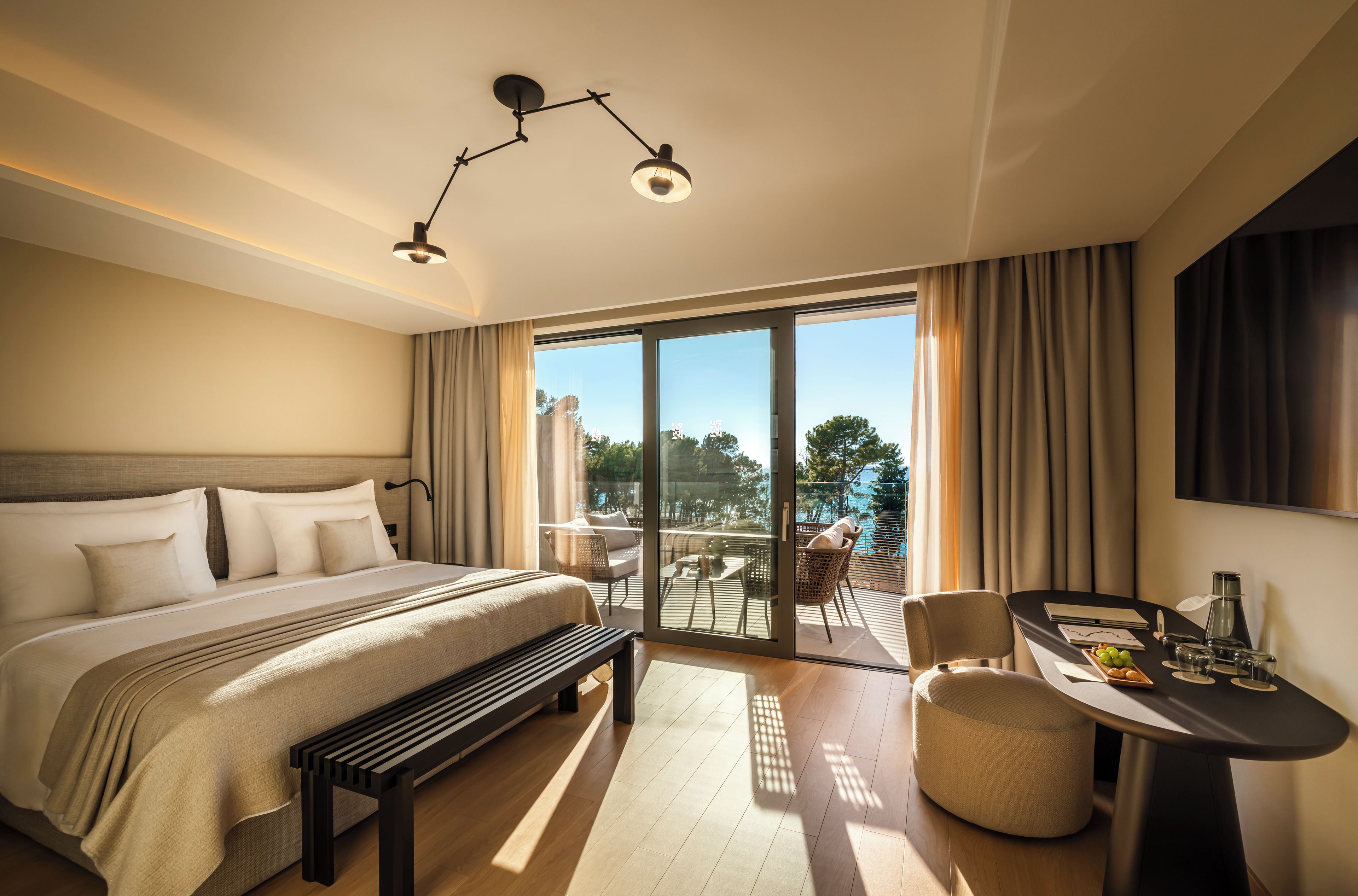 Een hotelkamer met een groot bed, een bureau met stoel, en een balkon met uitzicht.