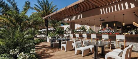 An outdoor patio with seating, a bar area, and palm trees.