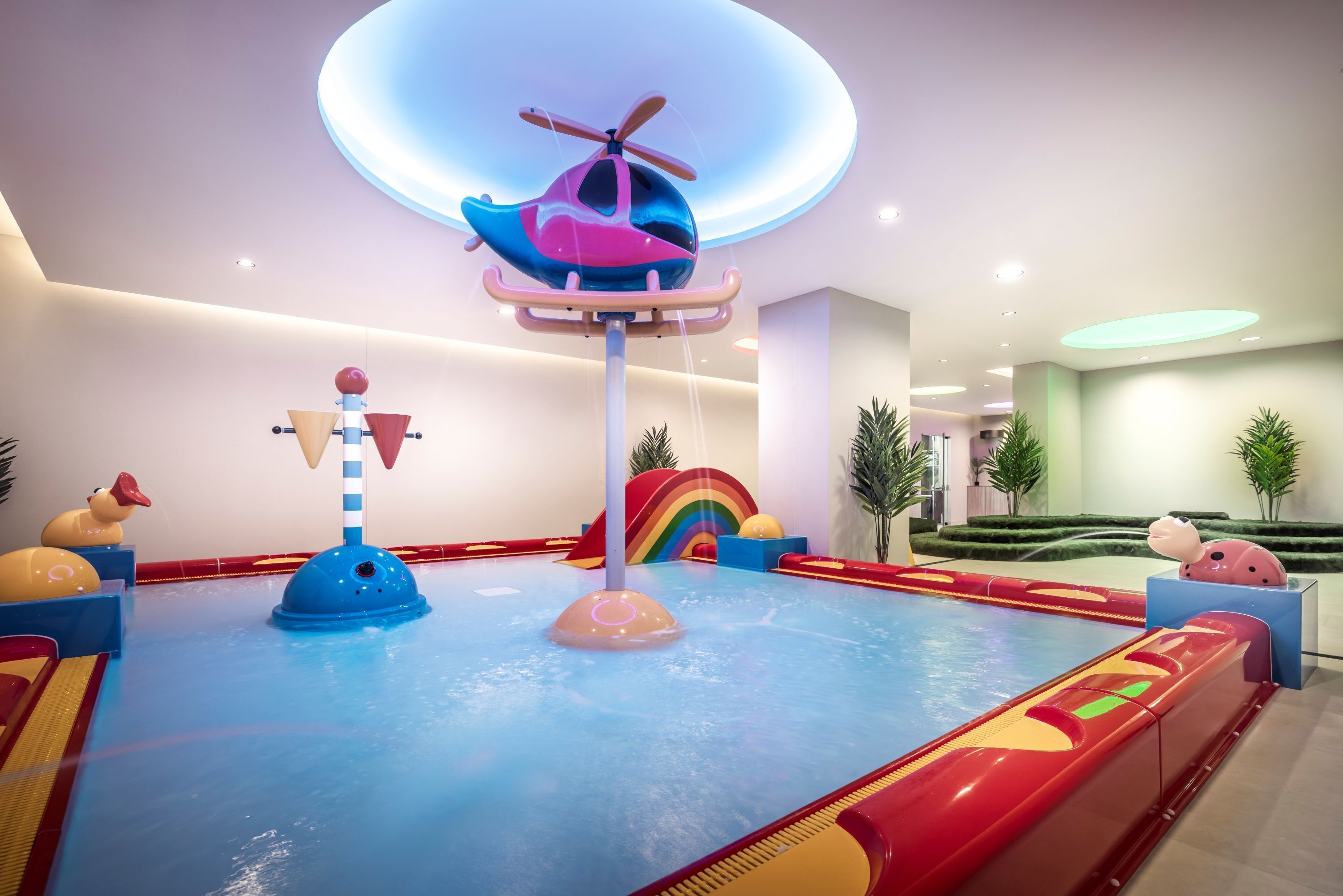 An indoor play area with a water slide, a helicopter ride, and colorful play structures.