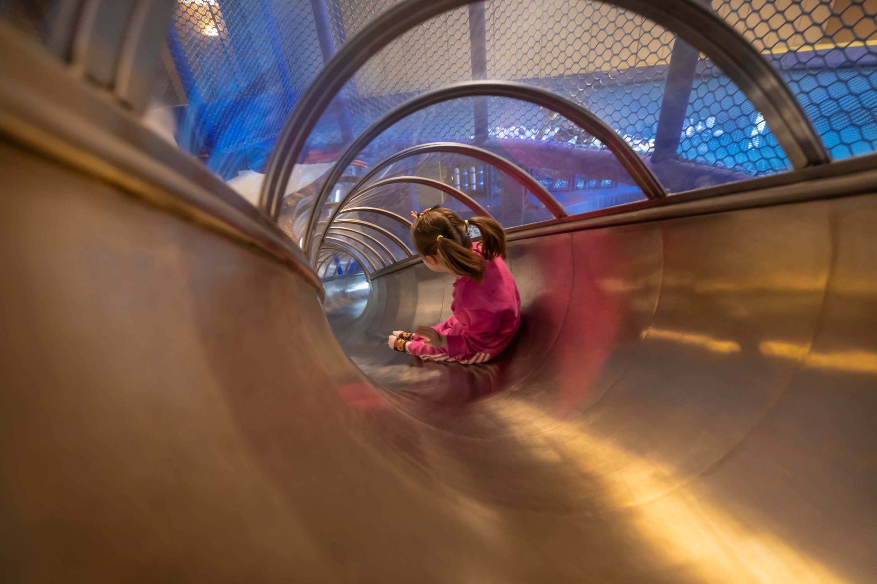 A child in a pink outfit sliding down a metallic spiral slide.