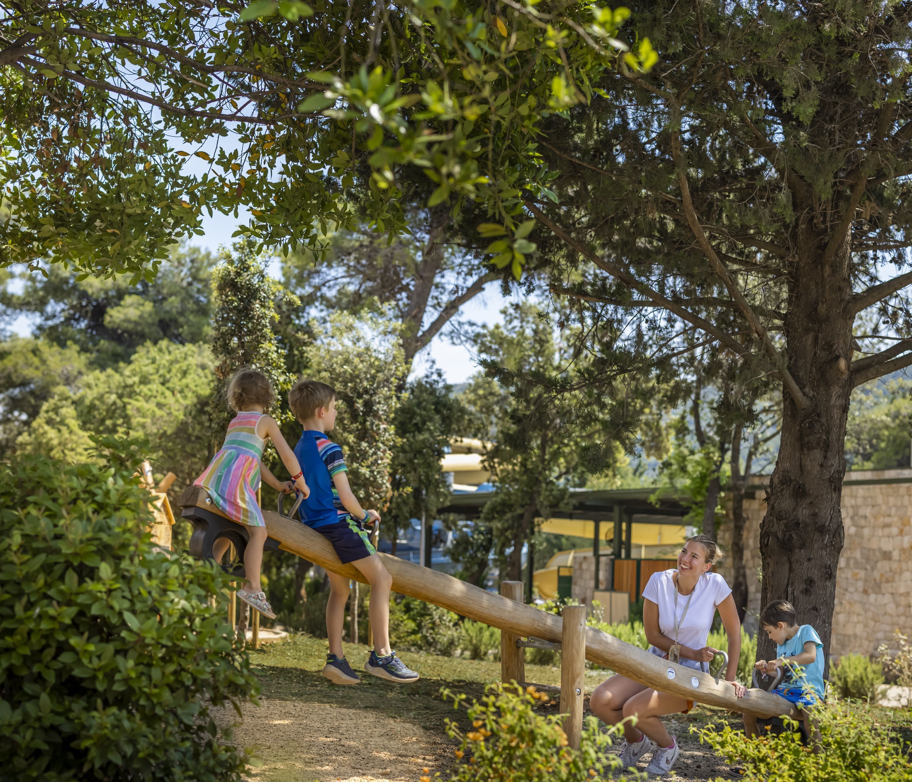 A seesaw with two children and a woman in a park.