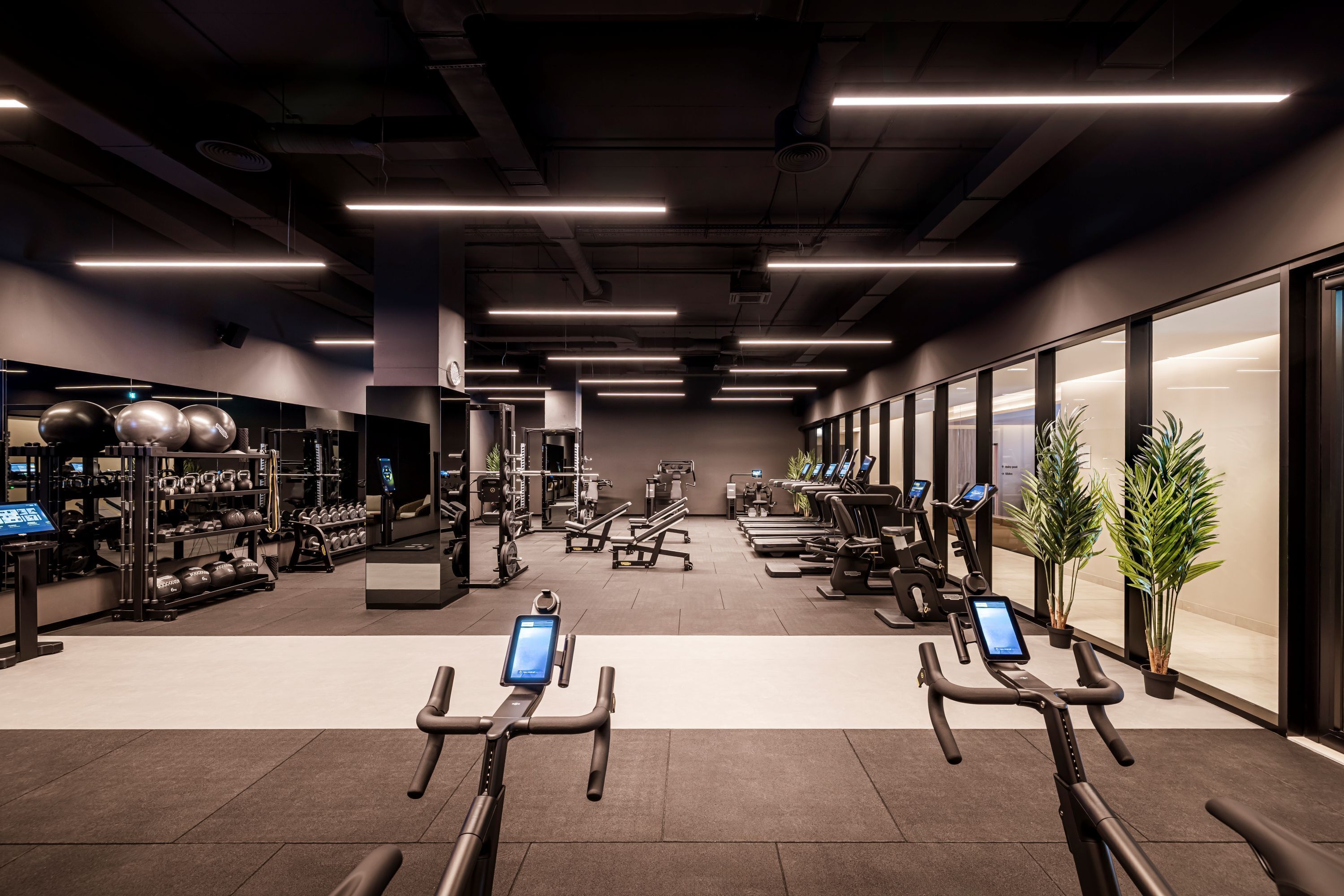 A modern gym with various exercise equipment, including treadmills and weight machines, and a digital interface on the machines.