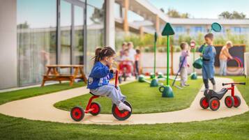 Niños jugando en un parque infantil con un edificio moderno al fondo.