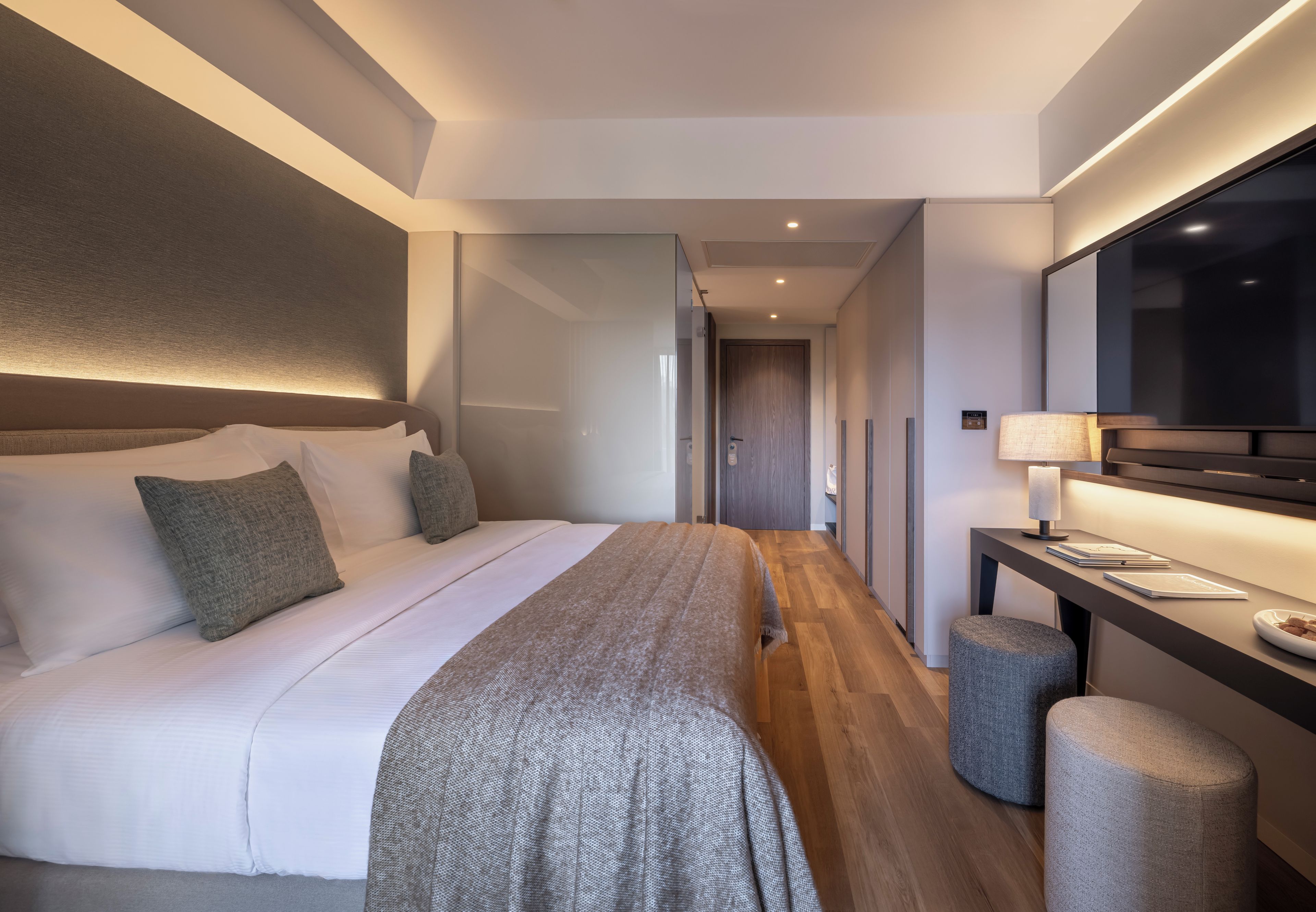 A modern hotel room with a large bed, a desk with a lamp, and a television.