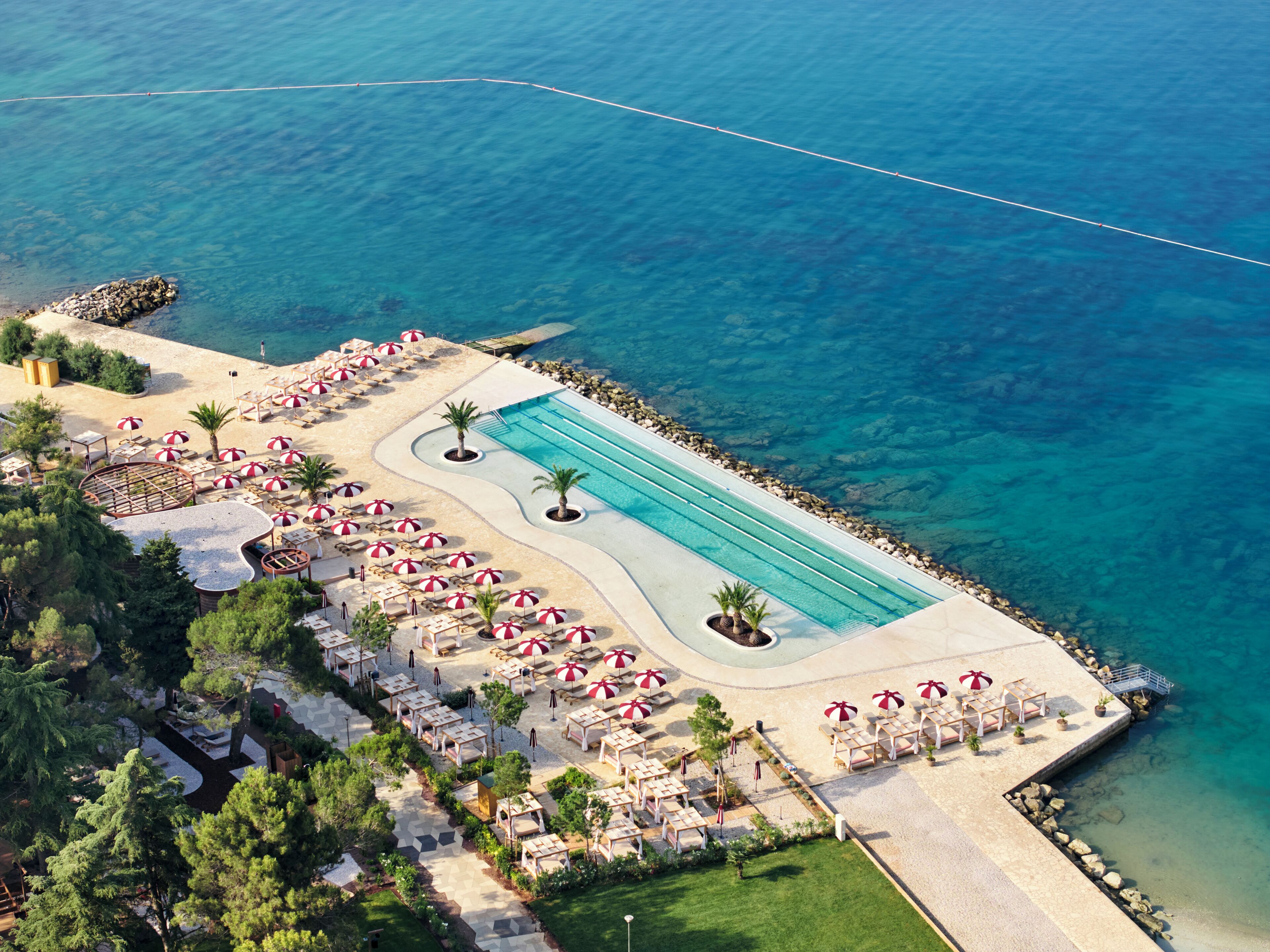 An aerial view of a resort with a swimming pool, sun loungers, and a beach area.