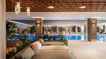 A modern indoor pool area with seating and plants.
