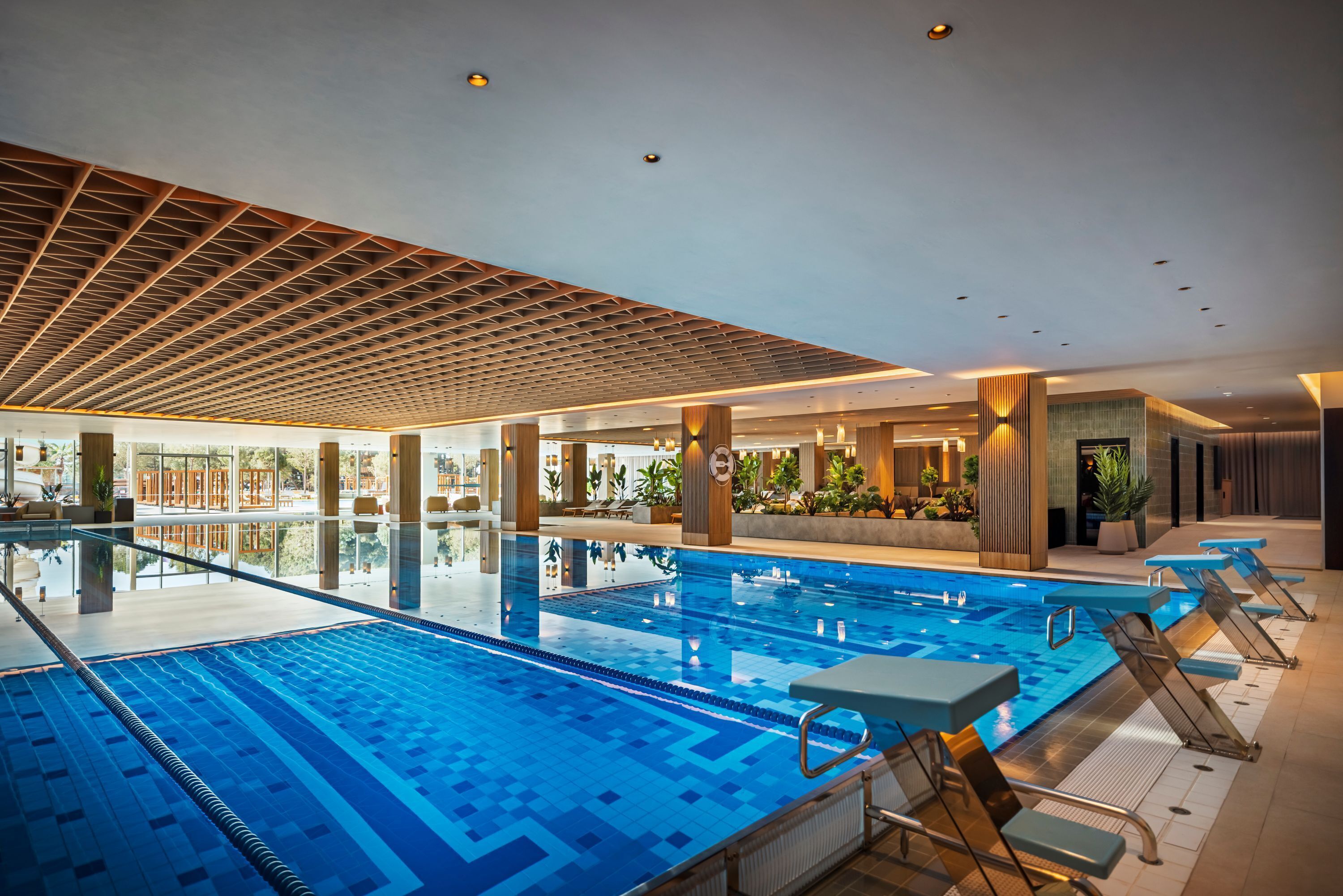 A large indoor swimming pool with clear water, surrounded by lounge chairs and a modern ceiling design.