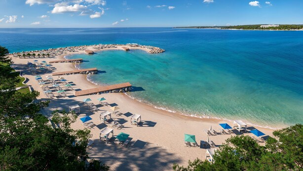 A beach resort with clear turquoise waters, a sandy beach, and numerous sun loungers. - Pical Resort , Valamar  Collection  (Porec)