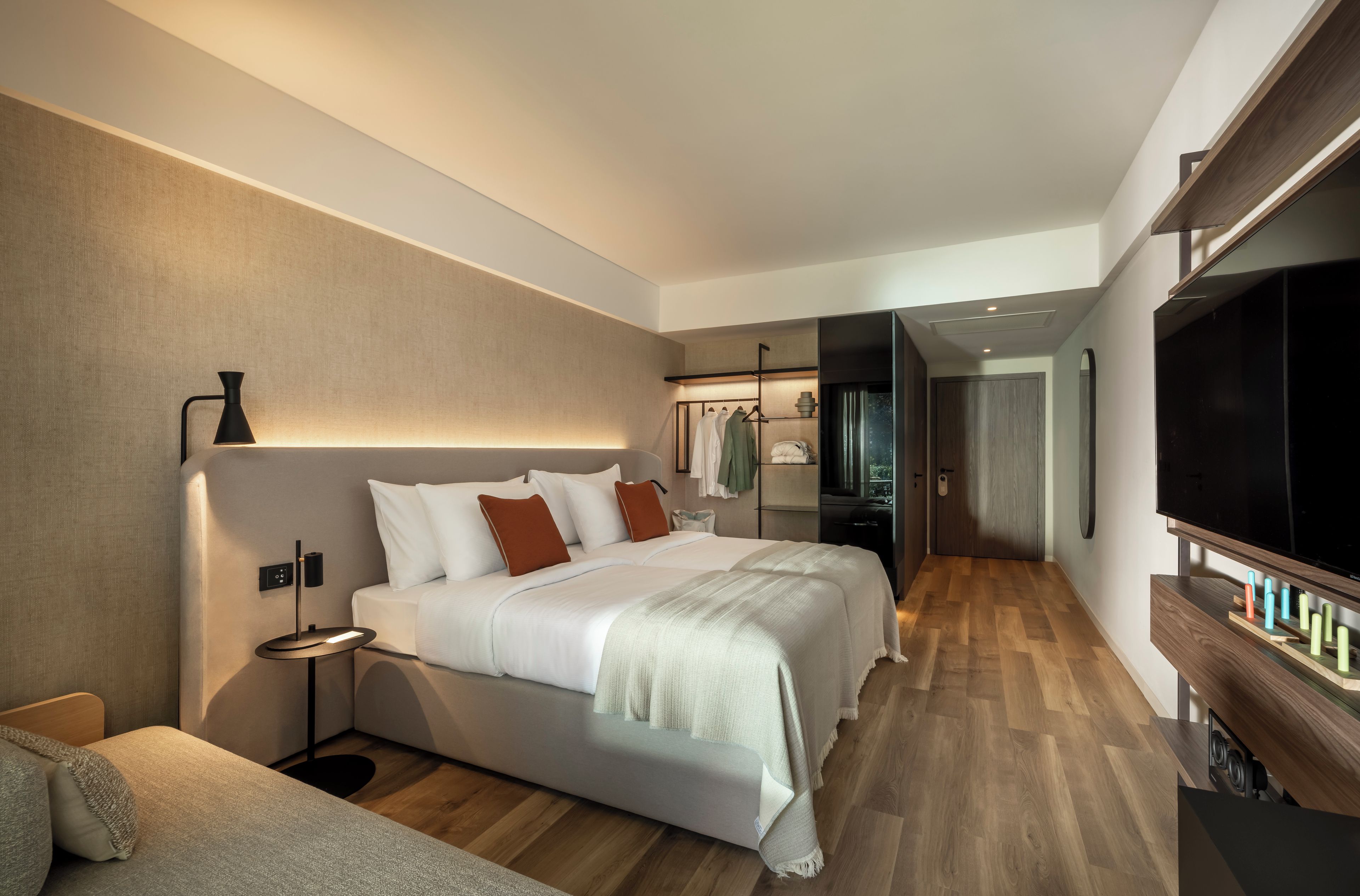 A modern hotel room with a large bed, bedside tables, a flat-screen TV, and a walk-in closet.