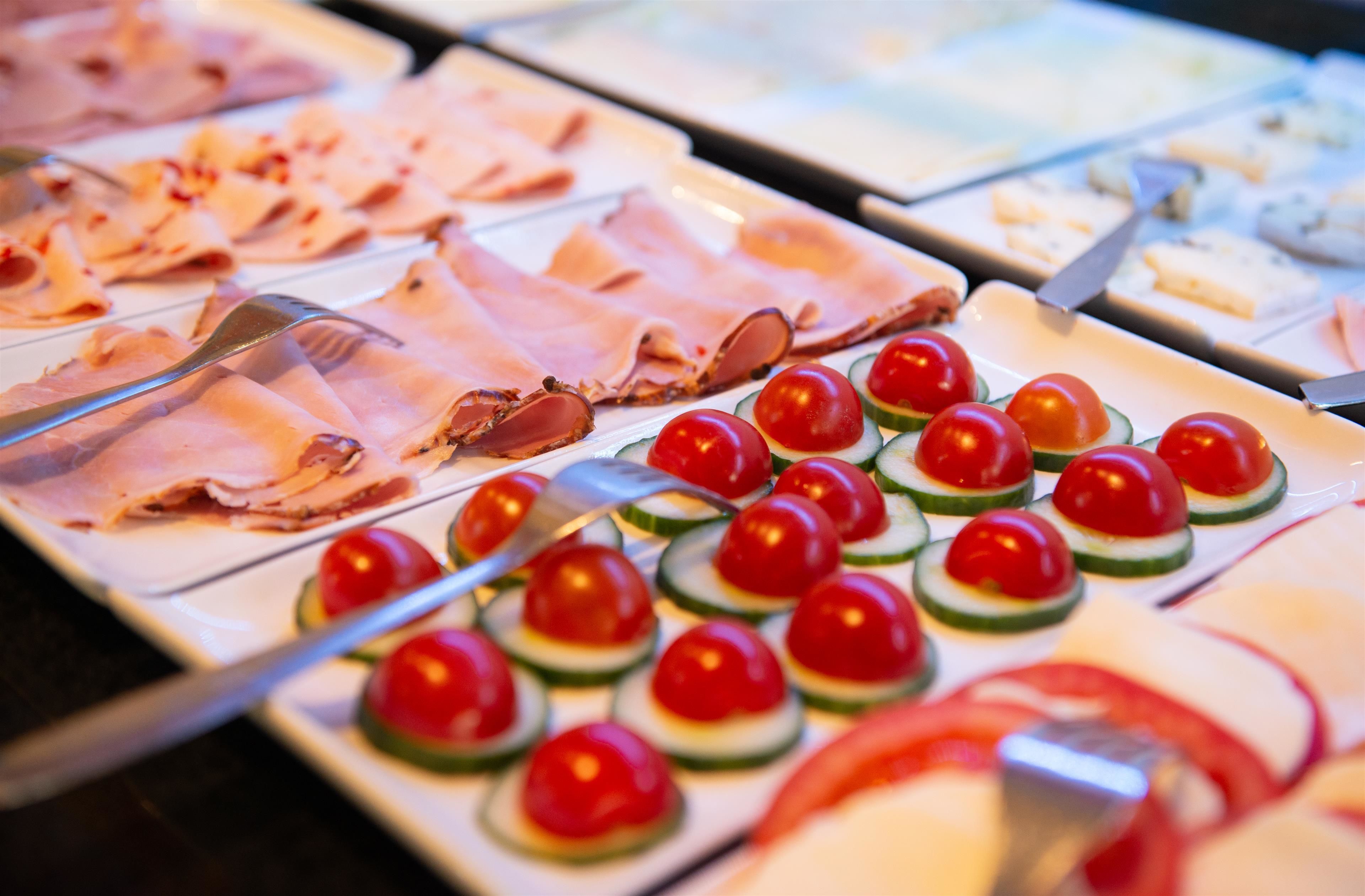 Ein Buffet mit verschiedenen Speisen, darunter Aufschnitt und Kirschtomaten auf Gurkenscheiben.
