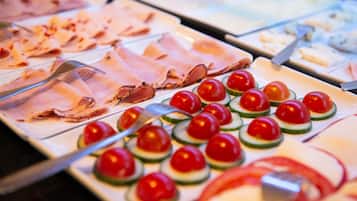 Ein Buffet mit verschiedenen Speisen, darunter Aufschnitt und Kirschtomaten auf Gurkenscheiben.