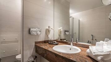 Un baño moderno con encimera de granito, lavabo blanco y un espejo grande.
