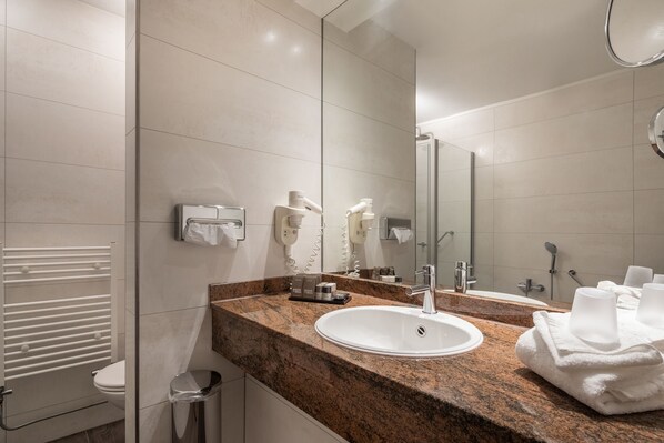 Un baño moderno con encimera de granito, lavabo blanco y un espejo grande.