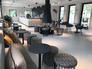 A modern interior with a bar area, seating arrangements, and large windows providing natural light. - Van der Valk De Gouden Leeuw (Voorschoten)