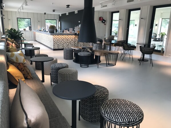 A modern interior with a bar area, seating arrangements, and large windows providing natural light. - Van der Valk De Gouden Leeuw (Voorschoten)