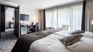 A hotel room with a large bed, a desk, a chair, a TV, and a window with curtains.
