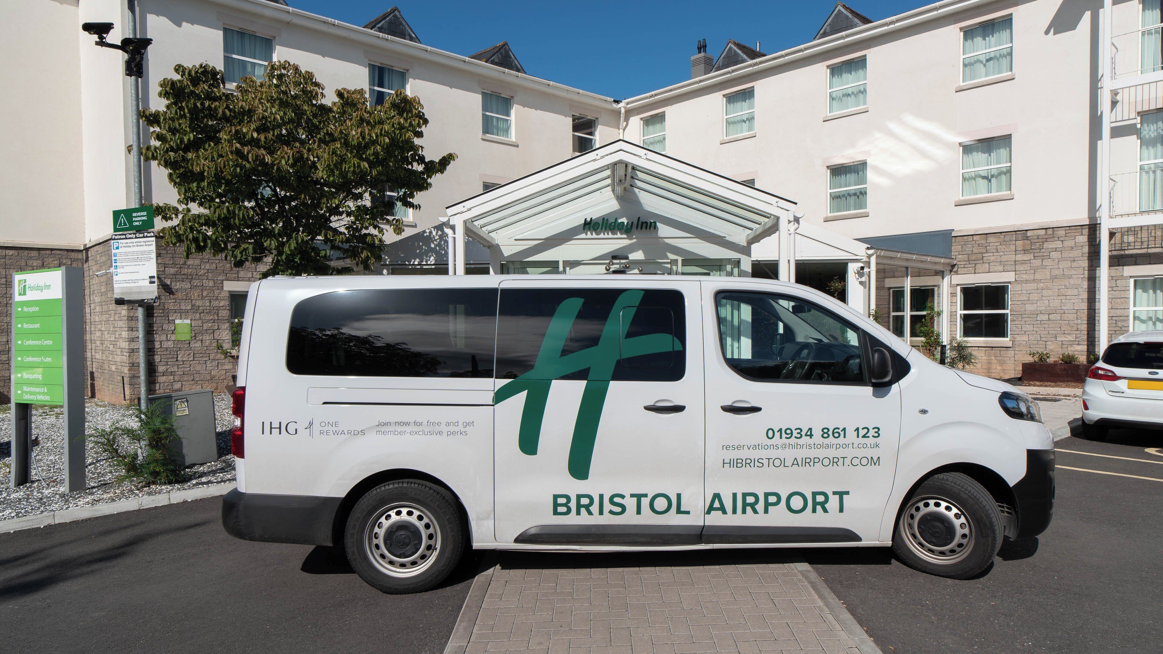 A white van parked in front of a building with a sign for Bristol Airport.