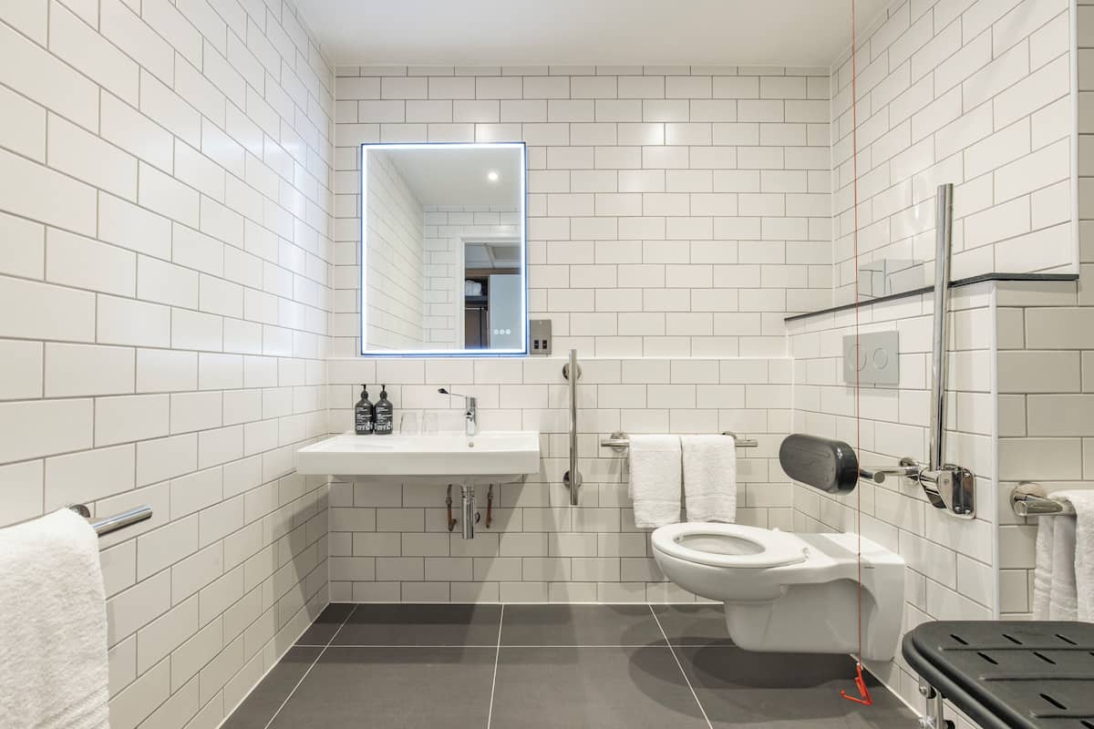 A modern bathroom with white subway tiles, a white sink, a toilet, and a mirror with a light.