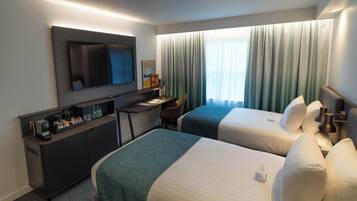 A hotel room with two beds, a desk, a television, and a minibar.