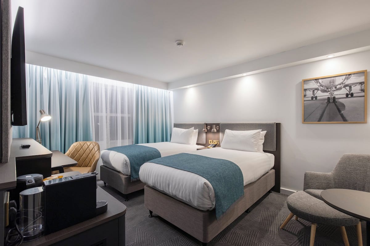 A hotel room with two beds, a desk, a chair, a TV, and a painting on the wall.
