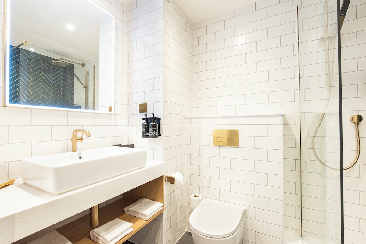 Een moderne badkamer met een wit wastafelmeubel, een spiegel, een toilet en een douchecabine met glazen wanden.