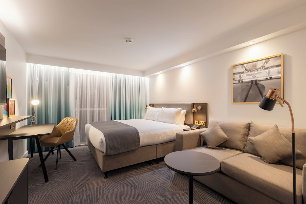A modern hotel room with a bed, a sofa, a desk, and a chair.