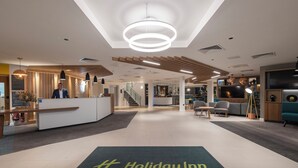 A modern hotel lobby with a reception desk, seating area, and a staircase leading to other floors. - Holiday Inn Bristol Airport by IHG (Bristol)