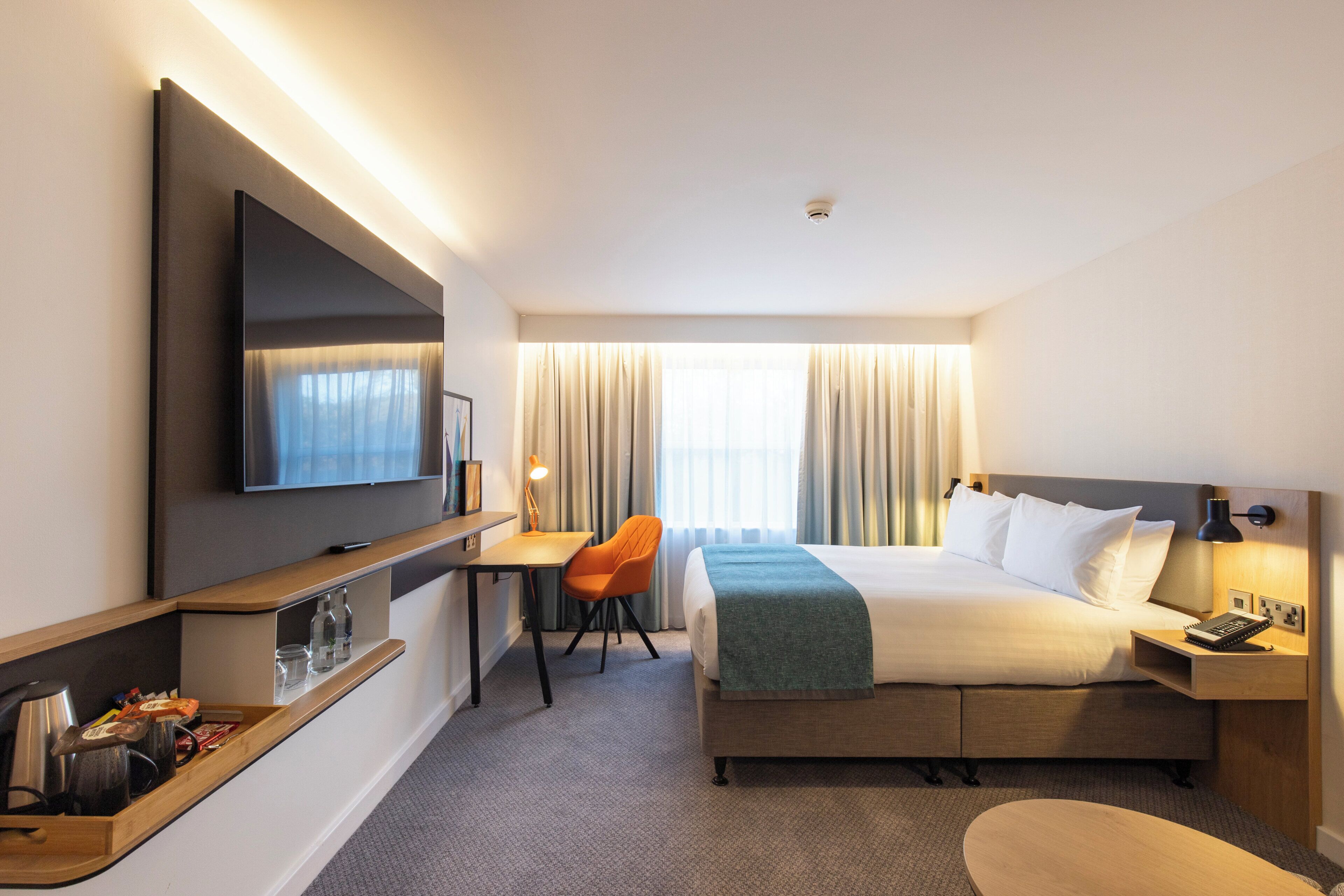 Une chambre d’hôtel équipée d’un lit, d’un bureau, d’une chaise, d’une télévision et d’une table de chevet avec une lampe.