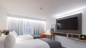 Et hotelværelse med to senge, et fjernsyn, et skrivebord med stol og en reol med genstande.