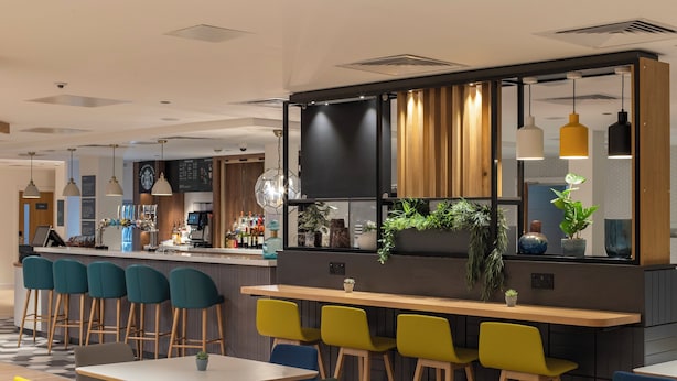 A modern bar area with stools, a counter, and a seating area with tables and chairs. - Holiday Inn Bristol Airport by IHG (Bristol)
