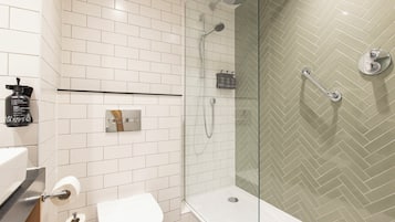 Baño con paredes de azulejos blancos, un inodoro, una ducha con puerta de cristal y una barandilla.