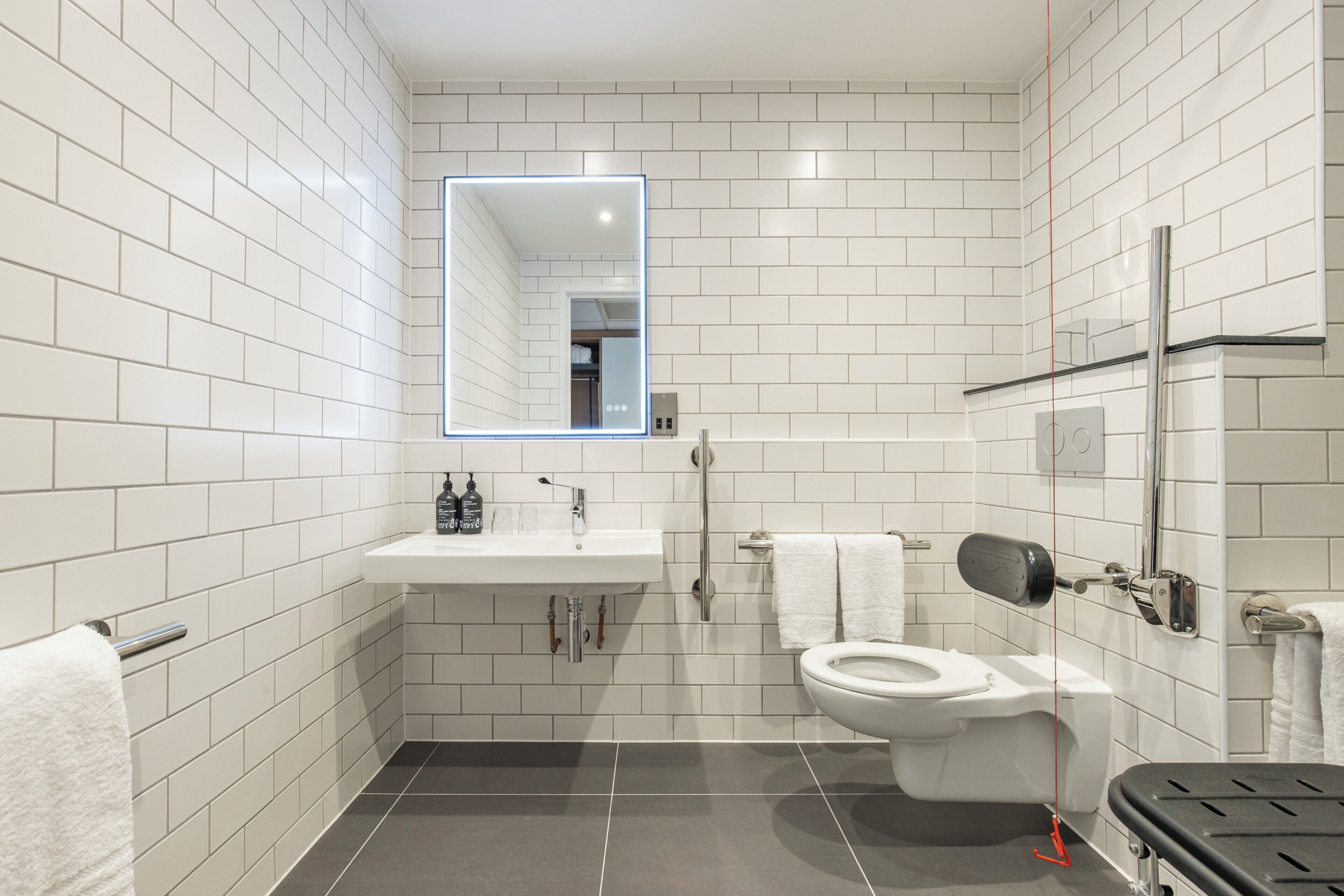 A modern bathroom with white subway tiles, a white sink, a toilet, and a mirror with a light.