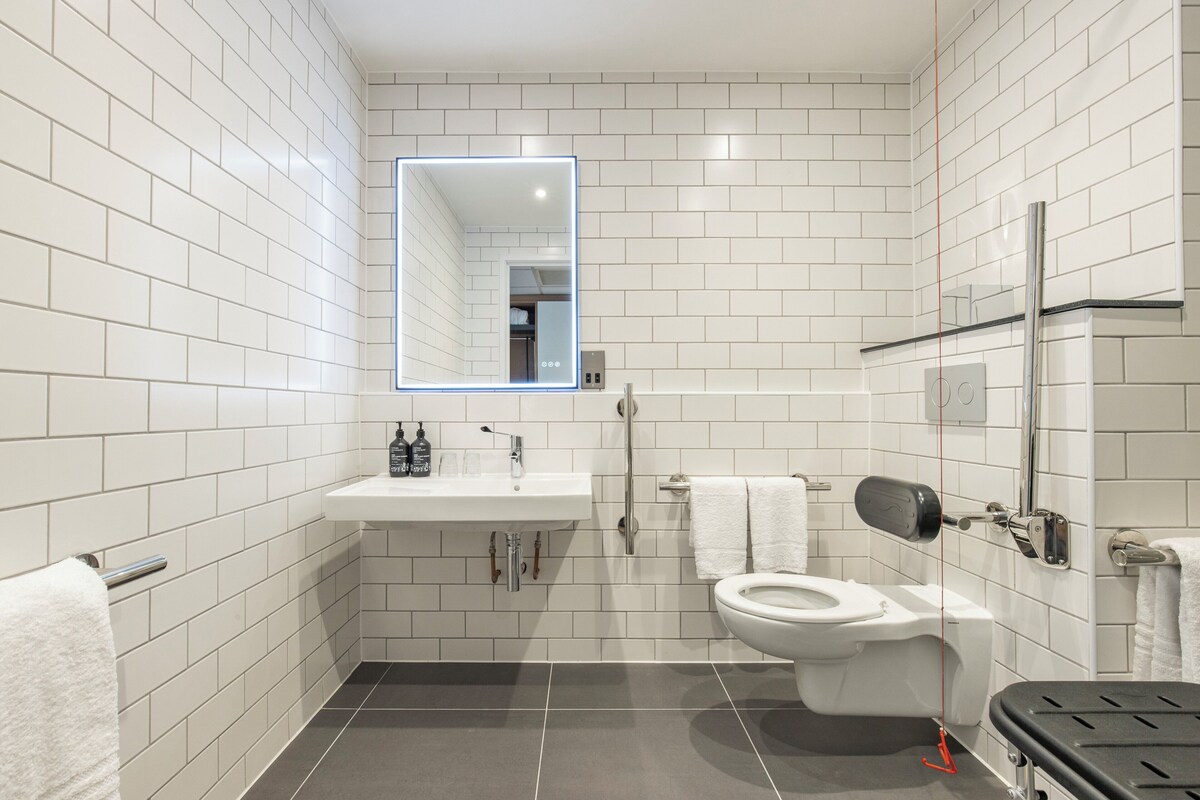 A modern bathroom with white subway tiles, a white sink, a toilet, and a mirror with a light.