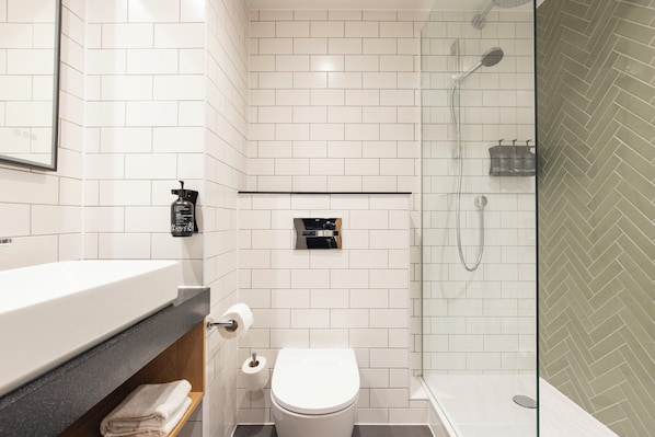 A modern bathroom with a white tiled shower, a toilet, and a sink with a towel rack.
