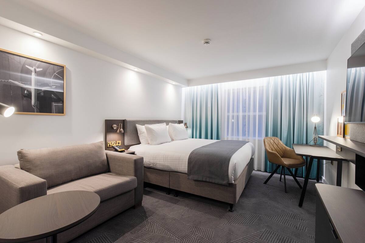 A modern hotel room with a bed, a sofa, a desk, and a chair.