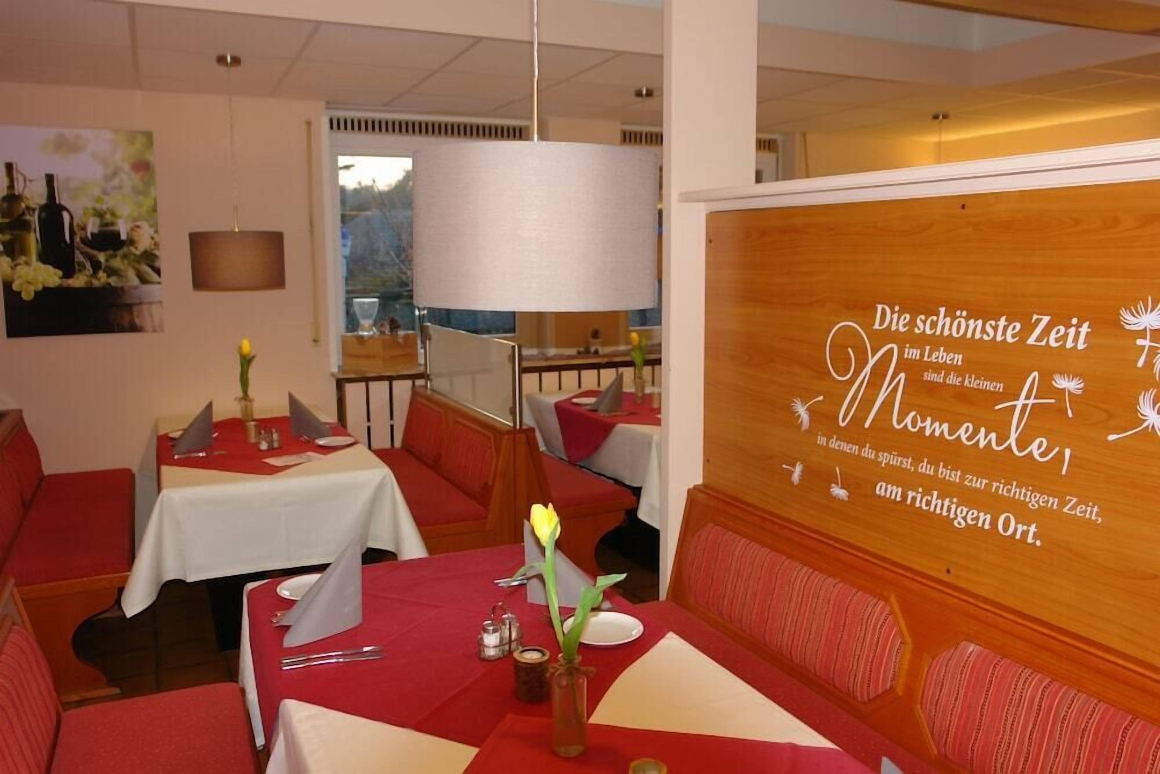 A restaurant interior with red tablecloths, wooden booths, and a wall with a motivational quote in German.