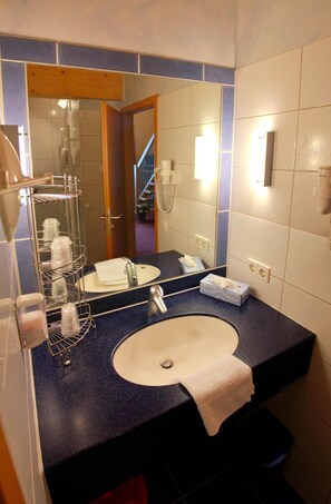 A bathroom with a sink, mirror, towel, and a shower area. - Hotel Froehlich (Kaiserslautern)