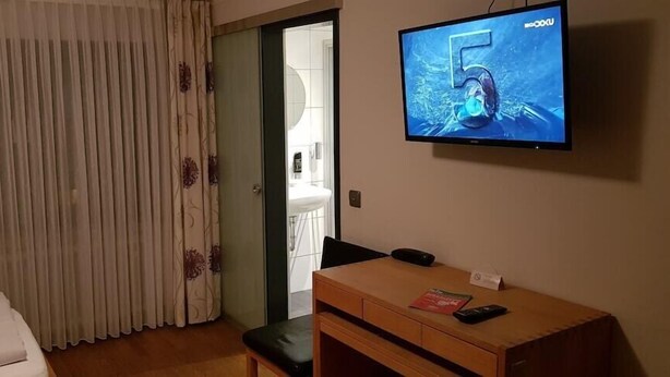 Habitación de hotel con cama, escritorio, televisor y baño visible a través de una puerta abierta.