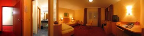 A hotel room with a bed, a desk, a chair, a TV, and a window with curtains. - Hotel Froehlich (Kaiserslautern)