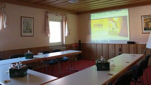 Un salón de conferencias con una larga mesa, sillas, una pantalla de proyector mostrando el sitio web de un hotel y una ventana con cortinas.