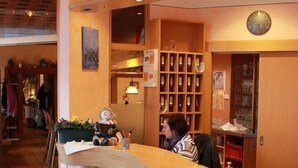 Zona de recepción con mostrador de madera, un reloj y un área de descanso con una persona.