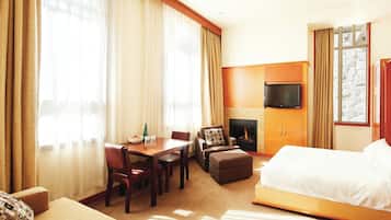 Une chambre d’hôtel équipée d’un lit, d’une télévision, d’une cheminée, d’un coin repas et offrant une vue sur l’extérieur.