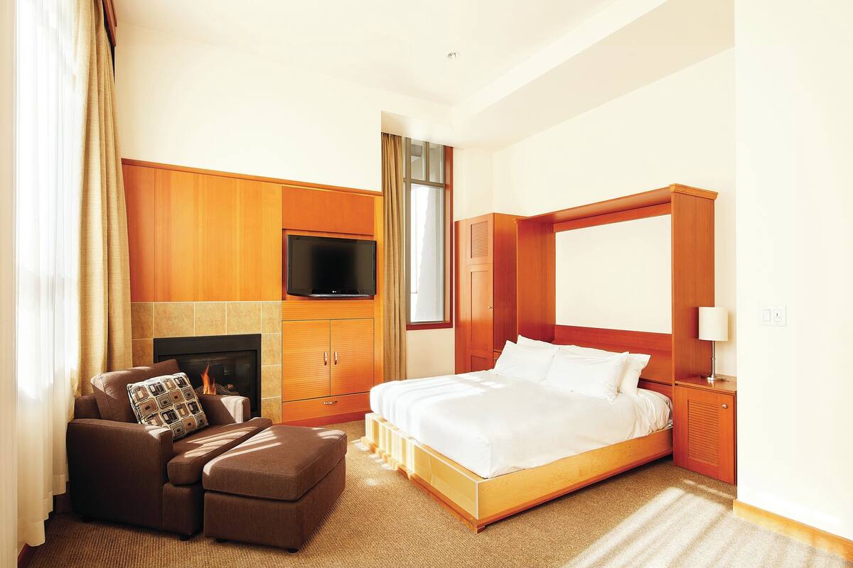 A hotel room with a bed, a sofa, a TV, and a fireplace.