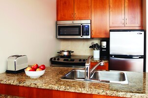 Una cocina con armarios de madera, un microondas de acero inoxidable, un tostador, un bol de manzanas, un fregadero y una estufa.