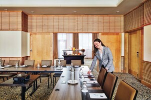 Un salón de conferencias con una larga mesa, sillas y un proyector. Se observa una zona de buffet al fondo, con comida y bebidas.