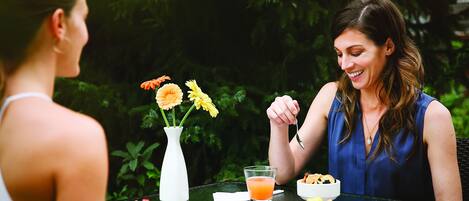 Two people sitting at an outdoor table with a meal, surrounded by greenery.