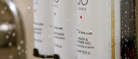 Three white bottles with black pumps, labeled 'Jo Loves', on a wall with water droplets.