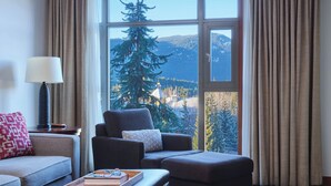 Una sala de estar moderna con un ventanal grande, un sofá, un sillón, una lámpara y una mesa de centro con libros y vasos.