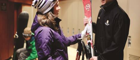 A person holding skis in a hallway with lockers.