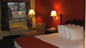 A hotel room with a large bed, a chair, a desk with a lamp, and a window with curtains. - Best Inn Booneville (Booneville)